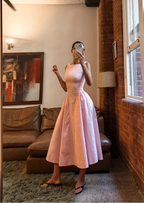 Woman in a pink dress taking a mirror selfie in a room with a large window and brick wall.